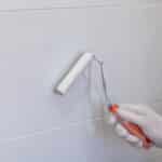 peinture de carreaux dans la cuisine dans la salle de bain peinture blanche avec un rouleau main dans le gant avec un rouleaux