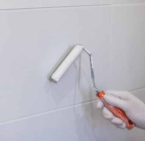 peinture de carreaux dans la cuisine dans la salle de bain peinture blanche avec un rouleau main dans le gant avec un rouleaux