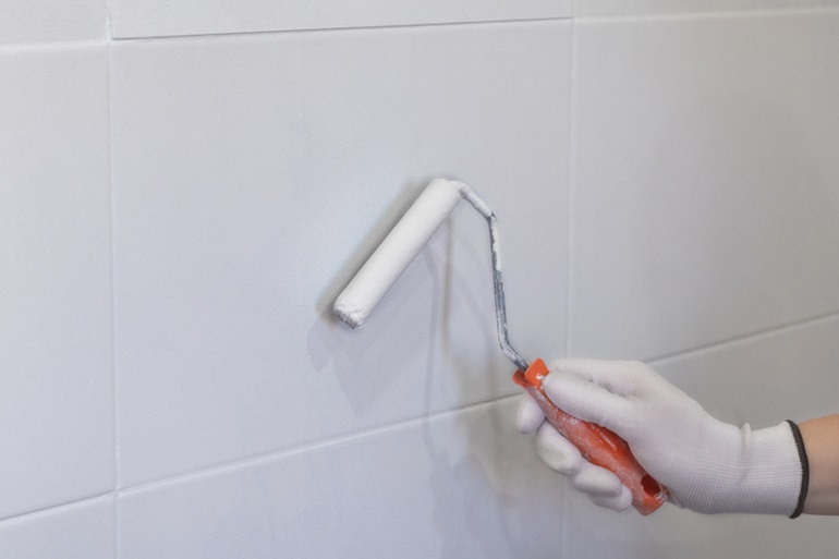 peinture de carreaux dans la cuisine dans la salle de bain peinture blanche avec un rouleau main dans le gant avec un rouleaux